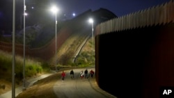 Jordanian migrants walk along the border walls separating Tijuana, Mexico, and San Diego, to apply for asylum with US authorities May 7, 2024, in San Diego.