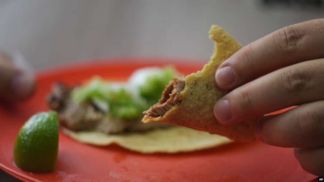A customer holds his partially eaten taco at the Tacos El Califa de León taco stand in Mexico City, May 15, 2024.