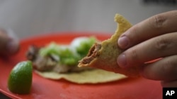 A customer holds his partially eaten taco at the Tacos El Califa de León taco stand in Mexico City, May 15, 2024.