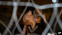 Una pareja de migrantes cargan a su bebé mientras se aproximan a una puerta en el muro fronterizo en las primeras horas del jueves 11 de mayo de 2023, después de cruzar desde Ciudad Juárez, México, hacia El Paso, EEUU.