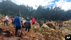 In this photo provided by the International Organization for Migration, people cross over the landslide area to get to the other side in Yambali village, Papua New Guinea, May 24, 2024.