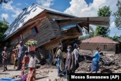 Warga berjalan di samping rumah yang hancur akibat banjir di Desa Nyamukubi, Provinsi Kivu Selatan, di Kongo, Sabtu, 6 Mei 2023.(AP/Moses Sawasawa)