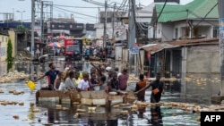 Sejumlah warga menyeberangi area yang terendam banjir di distrik Pompage di Kinshasa, Kongo, pada 9 Januari 2024. (Foto: AFP/Arsene Mpiana)