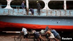 Bangladeshi laborers pull a cart carrying a ferry propeller in a dockyard in Dhaka.