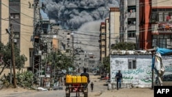 Una nube de humo se levanta tras una explosión mientras un hombre conduce un carro tirado por animales cargado de bidones en Nuseirat, en el centro de la Franja de Gaza, el 17 de abril de 2024.