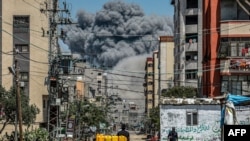 A cloud of smoke erupts down the road from an explosion as a man drives an animal-drawn cart loaded with jerrycans in Nuseirat in the central Gaza Strip on April 17, 2024.