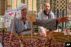 Seorang penjual kurma berbicara dengan pembelinya di pasar Sayyeda Zeinab menjelang Ramadan, di Kairo, Mesir, Selasa, 21 Maret 2023. (AP Photo/Amr Nabil)