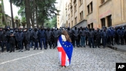 A demonstrator with draped Georgian national and EU flags stands in front of police blocking the way to the Parliament building, during an opposition protest against what has been dubbed "the Russian law," in the center of Tbilisi, Georgia, May 14, 2024.