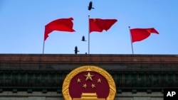 Birds fly past flags fluttering in the wind near the Chinese national emblem outside the Great Hall of the People in Beijing, March 3, 2023.