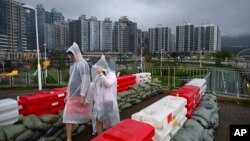People in rain coats walk past sandbagged barricades set up for Typhoon Saola as it passes through Lei Yue Mun district in Hong Kong on Sept. 2, 2023.