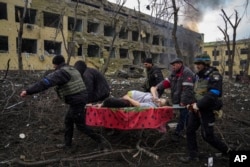 FILE - Ukrainian emergency workers and police evacuate an injured pregnant woman after a maternity hospital was damaged by a Russian airstrike in the Ukrainian city of Mariupol on March 9, 2022.