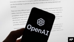 The OpenAI logo is seen on a mobile phone in front of a computer screen displaying output from ChatGPT, March 21, 2023, in Boston. (AP Photo/Michael Dwyer, File)