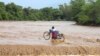 A man carrying his bicycle crosses through a flooded Muuoni River, where 8 people are said to have drowned overnight while crossing the river at Mukaa area, Makueni county, Kenya&#39;s Eastern region, Friday November 24, 2023. Flood-related death toll increased as heavy rains continued to pound across East Africa.&nbsp;