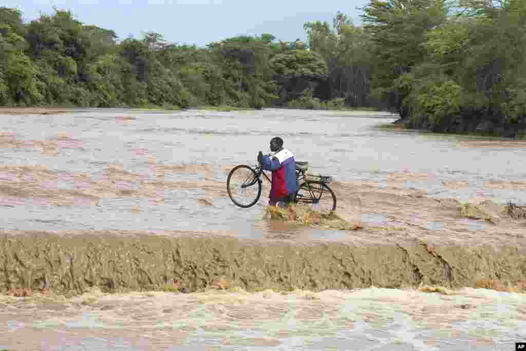 A man carrying his bicycle crosses through a flooded Muuoni River, where 8 people are said to have drowned overnight while crossing the river at Mukaa area, Makueni county, Kenya&#39;s Eastern region, Friday November 24, 2023. Flood-related death toll increased as heavy rains continued to pound across East Africa.&nbsp;