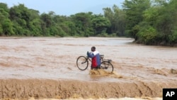 A man carrying his bicycle crosses through a flooded Muuoni River, where 8 people are said to have drowned overnight while crossing the river at Mukaa area, Makueni county, Kenya&#39;s Eastern region, Friday November 24, 2023. Flood-related death toll increased as heavy rains continued to pound across East Africa.&nbsp;