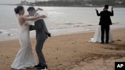 FILE - Wedding couples pose for photos on a beach in Qingdao in eastern China's Shandong province on Friday, April 19, 2024. (AP Photo/Ng Han Guan)