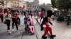 FILE - Visitors follow the Mickey Mouse character for photos at Disneyland in Anaheim, California, Jan. 22, 2015.