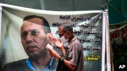 FILE - A protester prays by a poster showing Hisham al-Hashimi, who was shot dead in Baghdad, July 20, 2020. An Iraqi court on May 7, 2023 issued a death sentence against the alleged killer of al-Hashimi, nearly three years after his assassination.