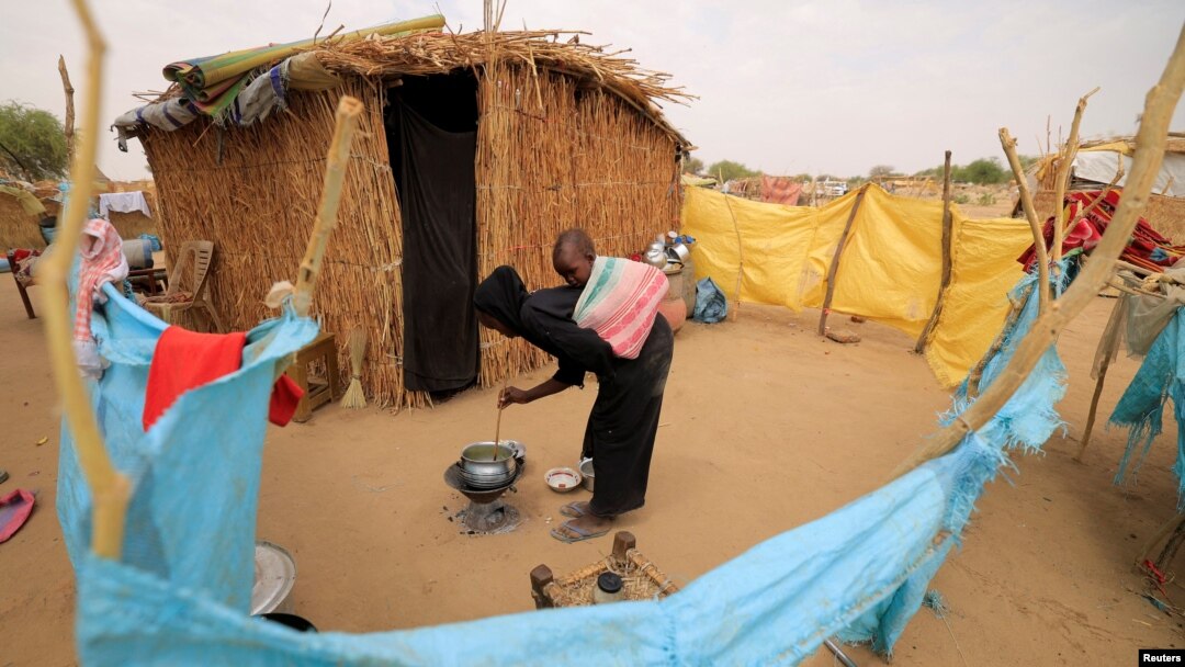 Fatna, 12, a Sudanese refugee girl who fled violence in Sudan's Darfur region, cooks as she carries her 2-year-old brother outside her shelter near the border between Sudan and Chad in Koufroun, Chad, May 10, 2023.