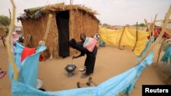 Fatna, 12, a Sudanese refugee girl who fled violence in Sudan's Darfur region, cooks as she carries her 2-year-old brother outside her shelter near the border between Sudan and Chad in Koufroun, Chad, May 10, 2023.