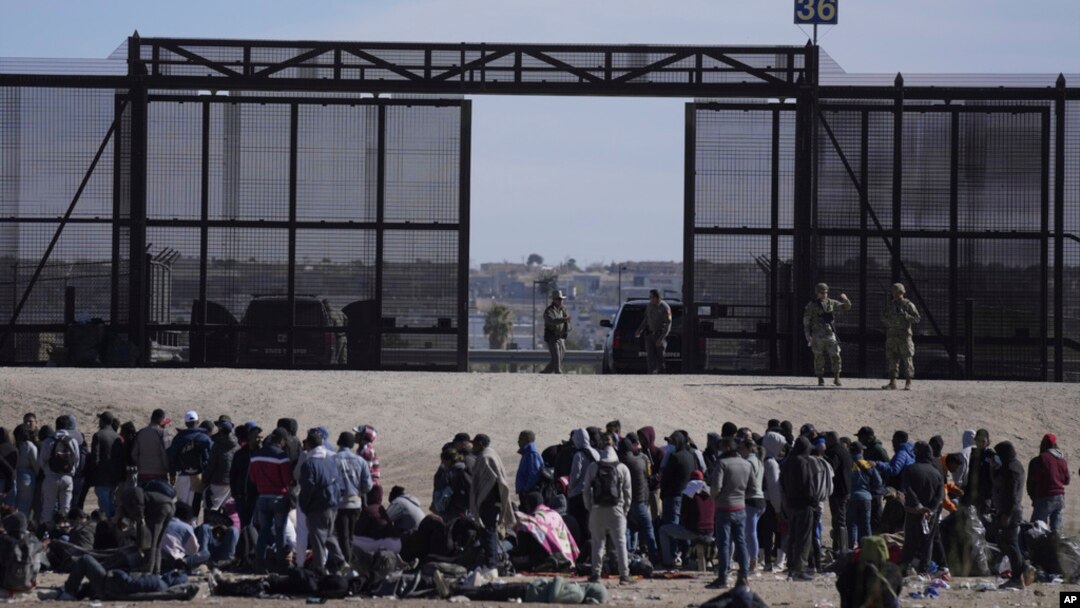 Migran yang melintasi perbatasan dari Meksiko ke AS menunggu di samping tembok perbatasan AS tempat agen Patroli Perbatasan AS berjaga, terlihat dari Ciudad Juarez, Meksiko, 30 Maret 2023. (Foto: AP)