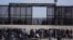 FILE - Migrants who crossed the border from Mexico into the US wait next to the US border wall where US Border Patrol agents stand guard, seen from Ciudad Juarez, Mexico, March 30, 2023. 