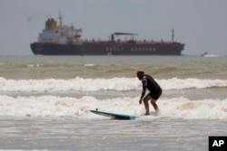 An oil tanker heads out to open water as a surfer takes advantage of waves ahead of Hurricane Beryl's arrival in Port Aransas, Texas, July 6, 2024.