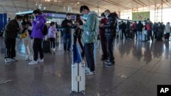 FILE - Masked travelers use their smartphones to fill in their health declaration after checking in at the international flight check in counter at the Beijing Capital International Airport in Beijing, Dec. 29, 2022.