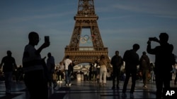 FILE - People use their smartphones near the Olympic rings displayed on the Eiffel Tower in Paris, June 7, 2024.