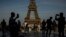 FILE - People use their smartphones near the Olympic rings displayed on the Eiffel Tower in Paris, June 7, 2024.