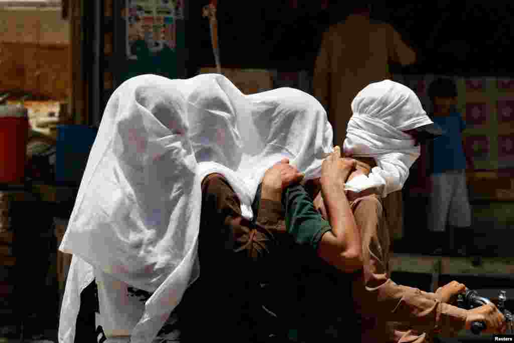 Men ride on a motorbike as they cover their heads with a wet cloth to cool off during a hot summer day, as the heatwave continues in Jacobabad, Pakistan, May 26, 2024.