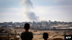 Dua anak laki-laki tampak memperhatikan asap yang mengepul dari sebuah araea di Rafah di saat pasukan Israel menyerang wilayah tersebut, pada 13 Mei 2024. (Foto: AFP)