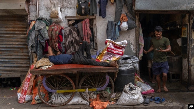 FILE - A man sleeps on a handcart, while clothes hang outside a bakery in Mumbai's Dharavi slum, India, Jan. 7, 2024.