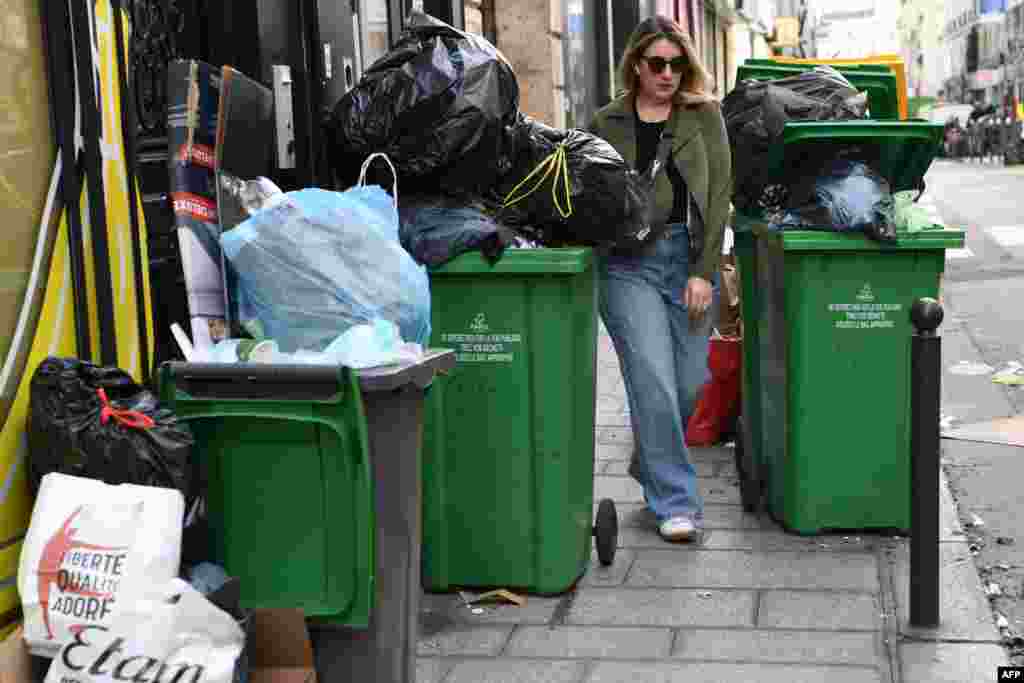 A pedestrian makes her way in between full waste bins in Paris' 2nd district as rubbish collectors strike against pension reforms, leaving many streets in the capital piled with stinking waste.