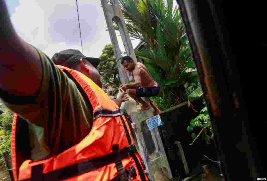 A flood victim hangs on a light post to receive lunch packets for his family from Sri Lankan army member on a flooded road in Kelaniya.