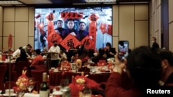 FILE - A woman takes pictures of a screen displaying the Spring Festival greetings by Chinese astronauts Fei Junlong, Deng Qingming and Zhang Lu from China's space station, during a Lunar New Year's Eve dinner in Beijing, China, January 21, 2023. (REUTERS/Florence Lo)