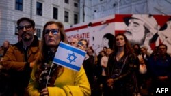 Seorang peserta aksi memegang bendera Israel dalam aksi mengenang korban serangan kelompok militan Hamas, yang digelar oleh Komunitas Yahudi di Wina, Austria, pada 11 Oktober 2023. (Foto: AFP/Joe Klamar)