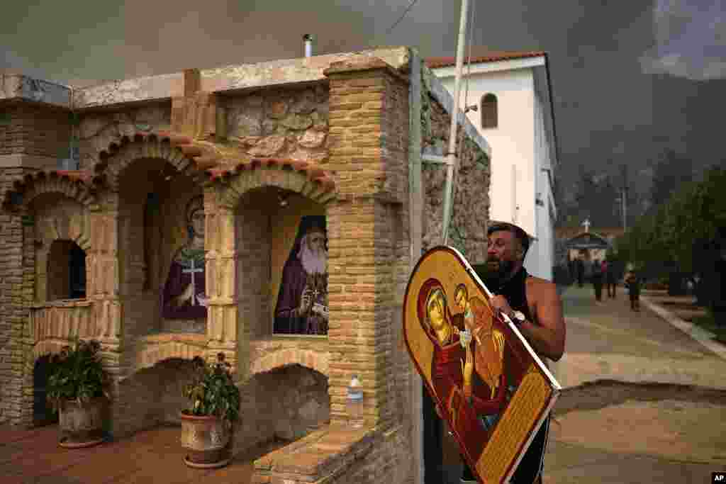 A man carries a saint Mary with Jesus icon to save it from a wildfire at Agia Paraskevi Christian Orthodox monastery in Acharnes a suburb of northern Athens, Greece.