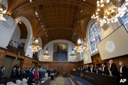 Delegasi Iran (kiri depan) dan delegasi AS (barisan depan belakang), berdiri saat para hakim mengambil tempat duduk mereka di Mahkamah Internasional, pengadilan tinggi PBB, di Den Haag, Belanda, 30 Maret 2023. (AP/Peter Dejong)