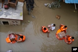 FILE - National Disaster Response Force (NDRF) personnel distribute relief material to flood affected people stuck in a low lying area around the river Yamuna in New Delhi, India, July 14, 2023. (AP Photo/Manish Swarup, File)