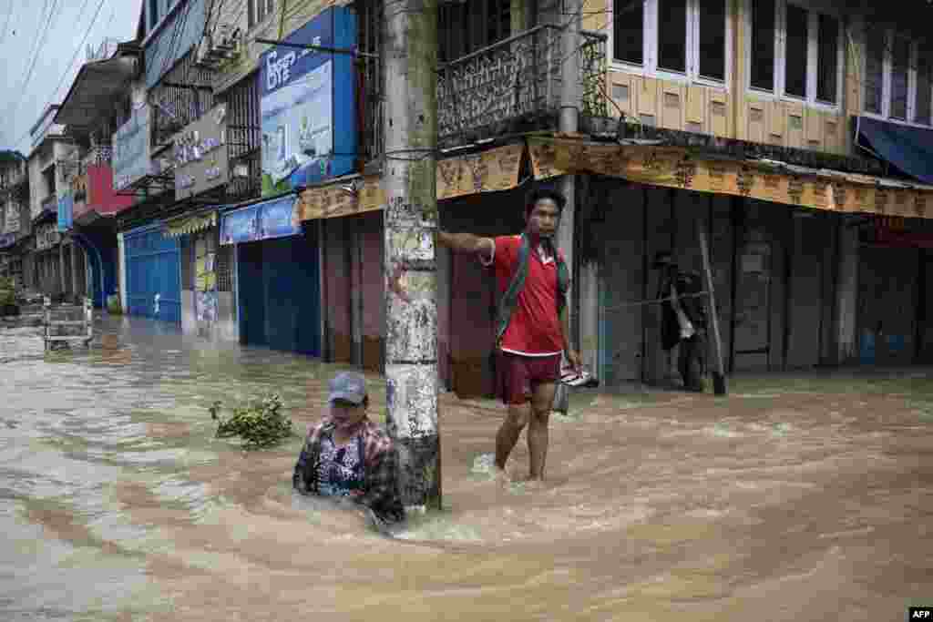 A woman sits next to a man along a flooded street following monsoon rains in Bago township, in the Bago region of Myanmar.