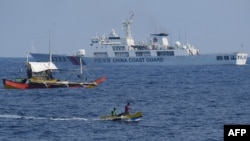 资料照：一艘中国海警船在南中国海有争议的海域监视菲律宾渔民的木船。（2024年5月16日 ）