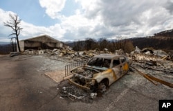 A charred car and the remains of the Swiss Chalet Hotel are pictured after being destroyed by the South Fork Fire in the mountain village of Ruidoso, New Mexico, June 22, 2024.