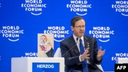 Israeli President Isaac Herzog gestures as he sits next to a photograph showing 10-month-old baby Kfir Bibas held by Hamas during a session of the World Economic Forum (WEF) meeting in Davos on January 18, 2024.