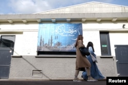 High school student Noha Fouad and her friend walks toward a classroom and in front of a banner that says 'Ramadan Kareem' in the courtyard of the Averroes school, Lille, France, March 19, 2024.