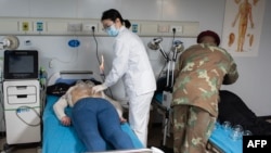 Seorang anggota tim medis militer China (kiri) dan seorang dokter medis (kanan) dari Dinas Kesehatan Militer Afrika Selatan (SAMHC) di atas kapal rumah sakit Chona Peace Ark yang berlabuh di Cape Town. 