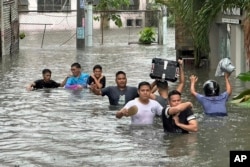 People walk through a street flooded from monsoon rains worsened by offshore typhoon Gaemi in Manila, Philippines, July 24, 2024.