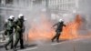 A riot police officer prepares to throw a stun grenade next to flames as clashes take place during a demonstration following the collision of two trains, near the city of Larissa, in Athens, March 5, 2023. 
