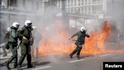 A riot police officer prepares to throw a stun grenade next to flames as clashes take place during a demonstration following the collision of two trains, near the city of Larissa, in Athens, March 5, 2023. 