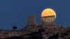 Bulan purnama tampak muncul dari balik kuil marmer kuno Poseidon di Tanjung Sounion, sekitar 70 Km (45 mil) selatan Athena, Yunani. (AP)&nbsp;